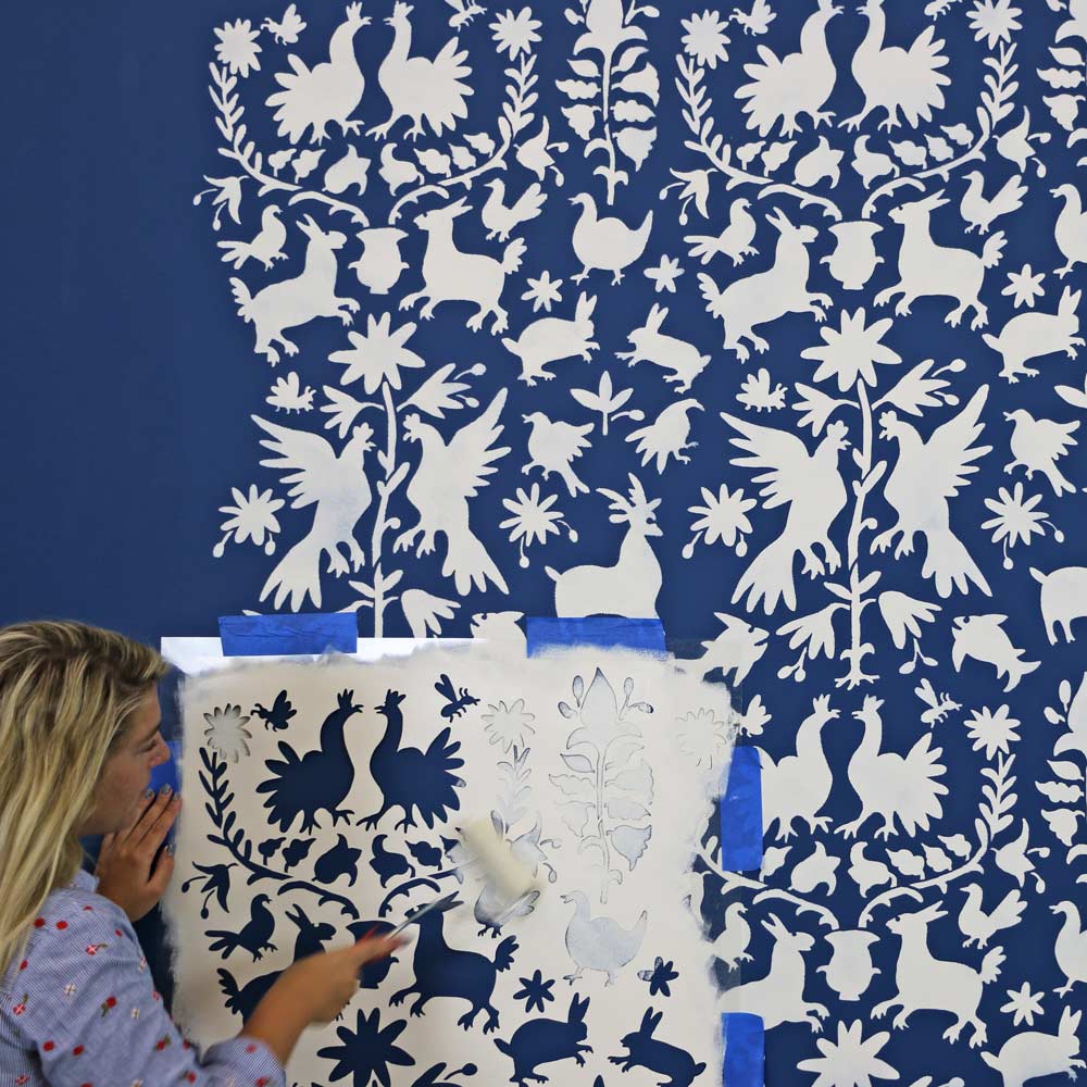 girl painting otomi wall stencil pattern on blue wall